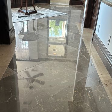 Shiny marble floor reflecting ceiling fan and windows in an elegant hallway.