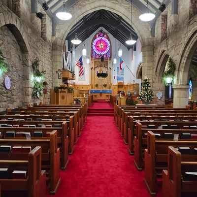 Interior of a church with wooden pews, red carpet, and a stained glass window.