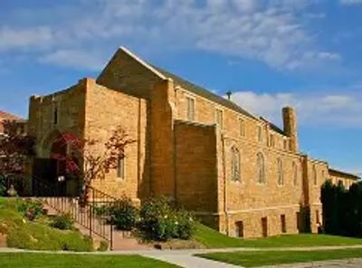 Historic stone building under a blue sky with surrounding greenery.