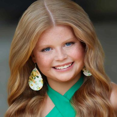 Smiling girl with long wavy hair and floral earrings.