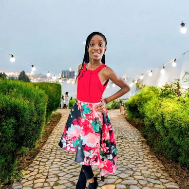 Girl in a red top and floral skirt posing outdoors on a cobblestone path.