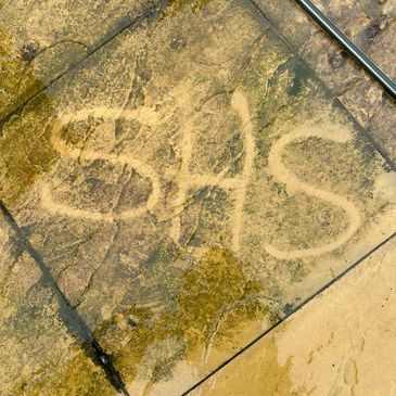 Letters 'SHS' drawn on a wet stone pavement.