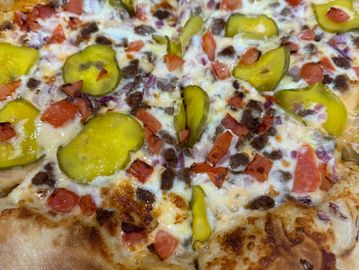 Pizza with pickles, tomatoes, and bacon bits.