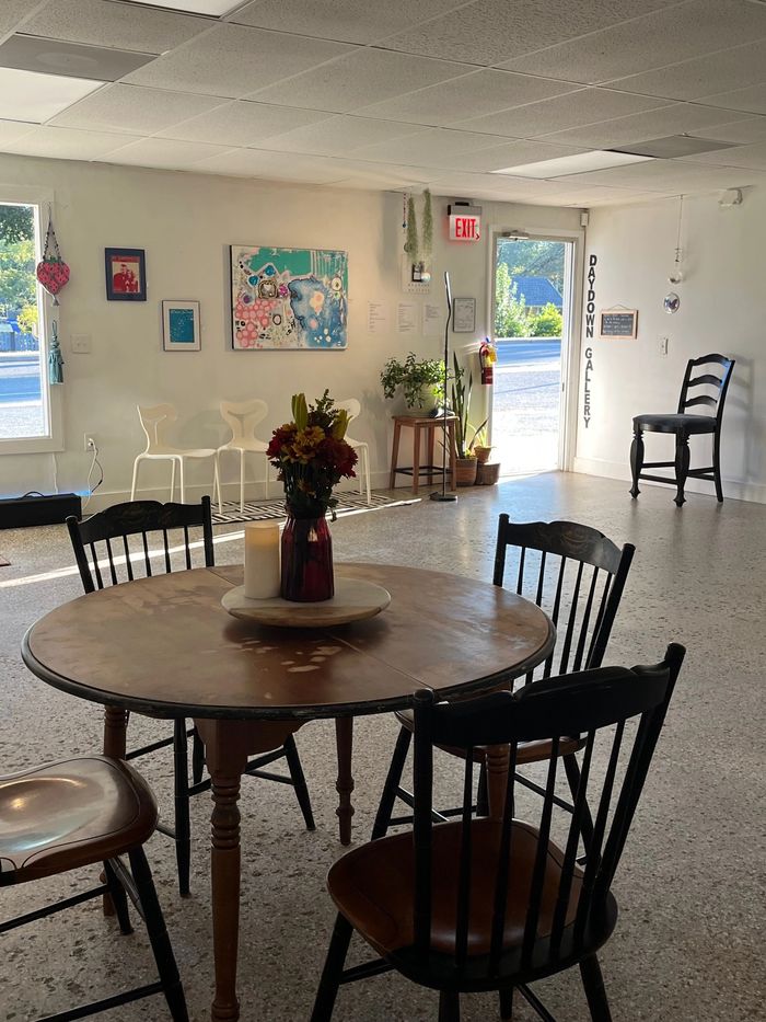 Cozy gallery space with wooden table, chairs, and art on walls.