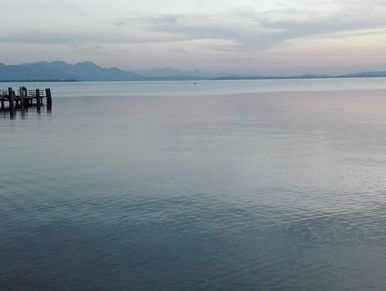 großer See bei Abenddämmerung vor einer Bergkulisse in der Ferne.