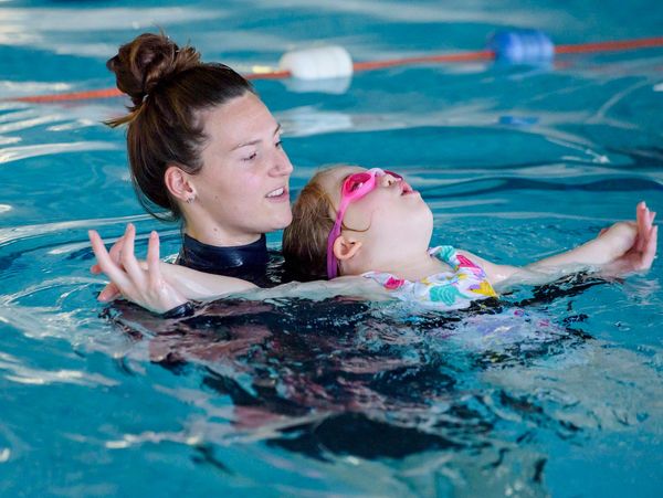 A swimming instructor helping a child to swim