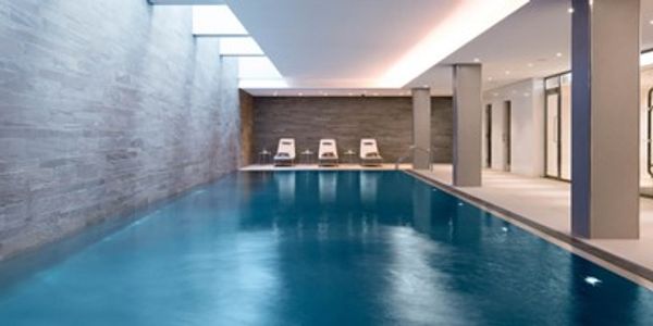 Modern indoor swimming pool with lounge chairs and soft lighting.