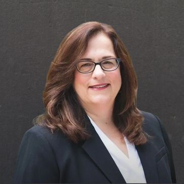 Professional woman with glasses and brown hair smiling against a dark background.