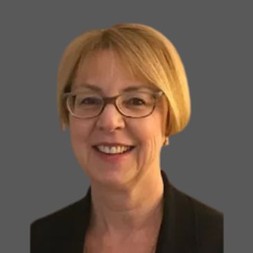 Smiling woman with glasses and short blonde hair against gray background.