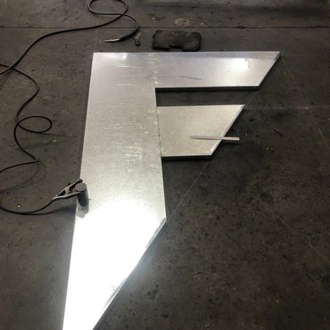 Metal sheet work on a dark workshop floor with welding equipment.