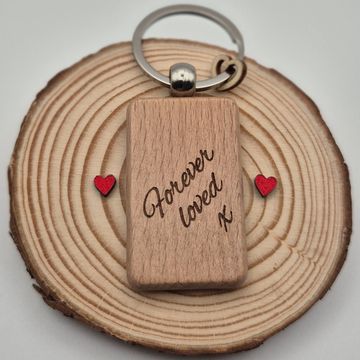 Wooden keychain with the inscription 'Forever loved' on a wooden slice with two small red hearts.