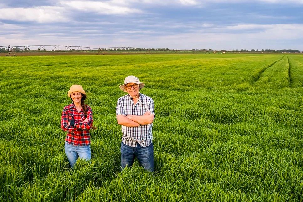 Father and daughter farmers in lush green farmland with the Rio Vista bridge in the background.