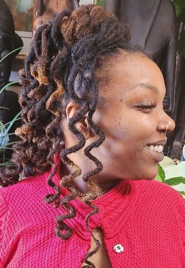 Woman with curly dreadlocks smiling in a red sweater.