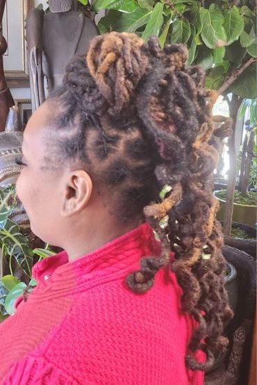 Woman with styled dreadlocks tied up, wearing a red sweater.