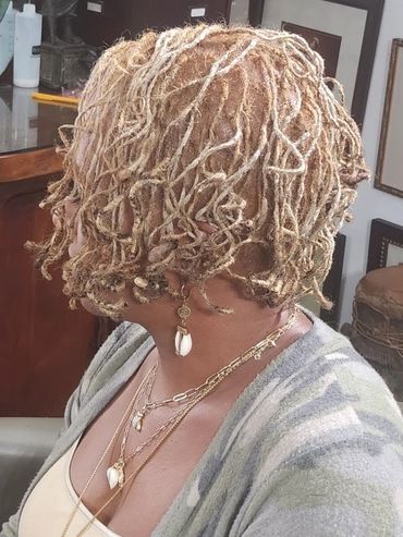 Woman with short, blonde dreadlocks and layered gold jewelry.