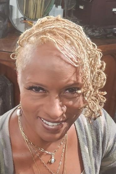 Smiling woman with blonde dreadlocks styled to one side.