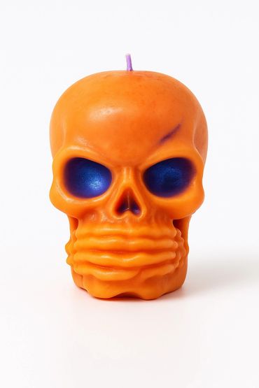 Vibrant orange skull-shaped soy candle with deep black eye sockets. Bold, spooky!