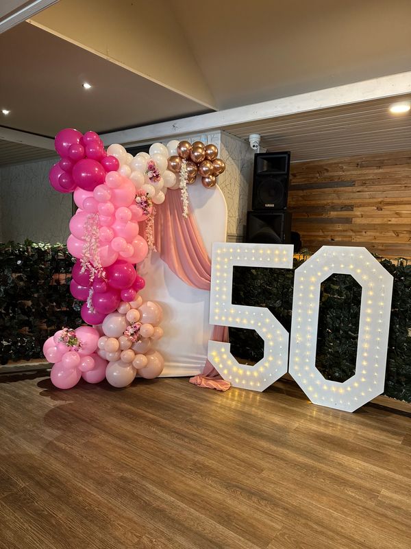 Decorative setup with pink balloon arch and large illuminated number 50.