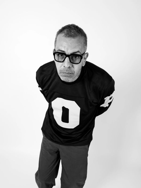 Man in black jersey with number zero looking up, hands behind back.
