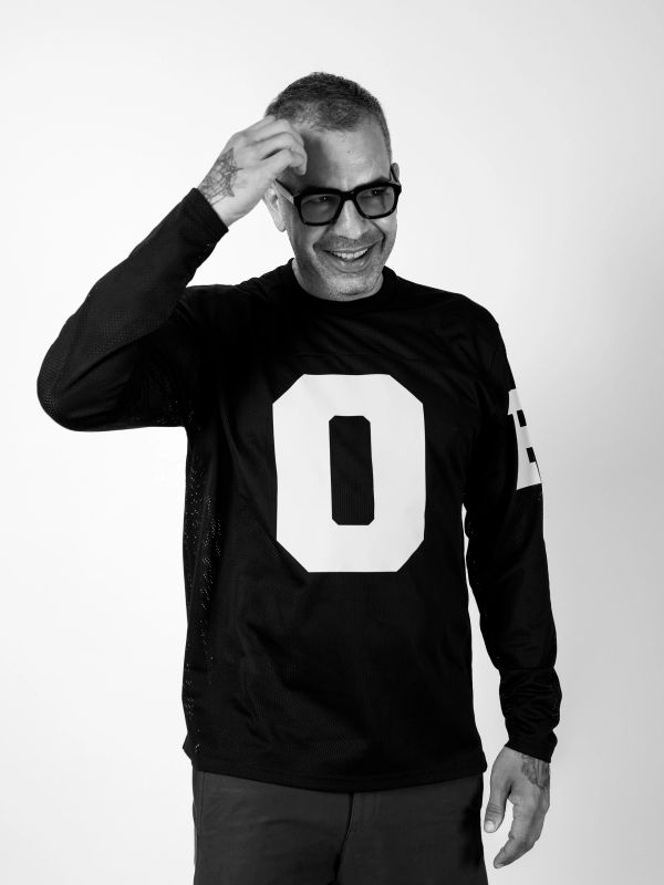 Man smiling and adjusting glasses wearing a black shirt with a large '0'.