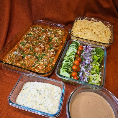 Home-cooked meal with meatballs, spaghetti, salad, rice, and sauce.