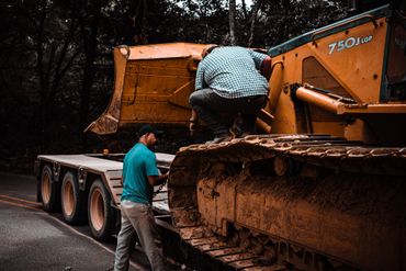 Two men working on securing a large construction excavator for transport.