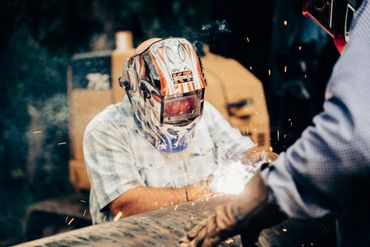A man welding metal wearing a protective helmet and shirt.