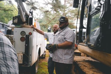 Two men working with heavy machinery outdoors, one holding a remote control device.