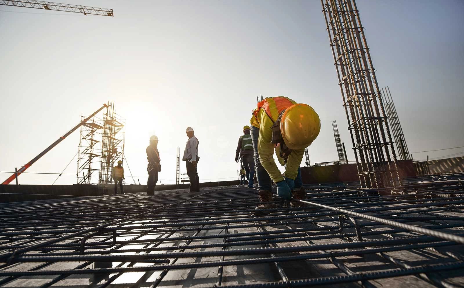 Construction workers securing steel rebar on a building site at sunset.