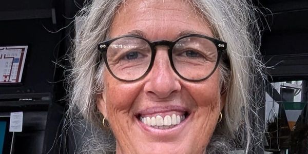 Smiling elderly woman with glasses and gray hair in a knitted green sweater.