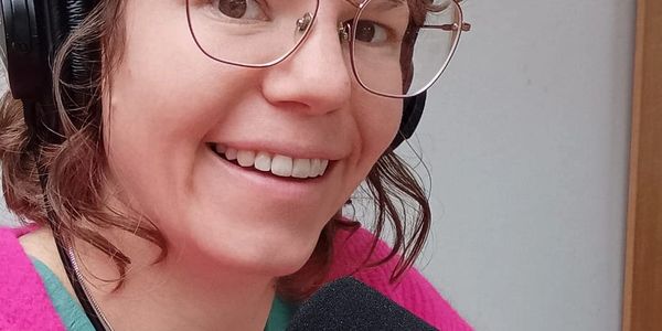 Woman wearing headphones and speaking into a microphone with audio mixer.