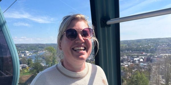Smiling woman in sunglasses enjoys a sunny gondola ride with scenic views.