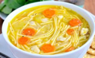 A bowl of chicken noodle soup with carrots and crackers.
