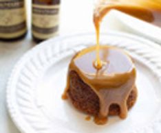 Caramel sauce being poured over a sticky toffee pudding on a white plate.