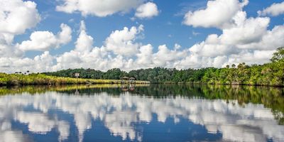 Calm river reflecting a blue sky with fluffy white clouds and green trees.