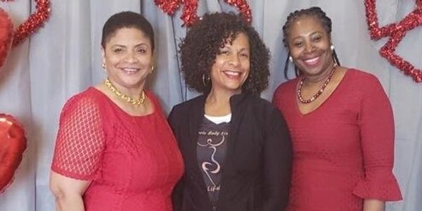 Three women smiling, two in red dresses and one in black jacket.