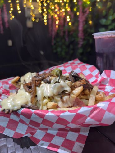 Melted cheese fries topped with mushrooms and a pepper on checkered paper.