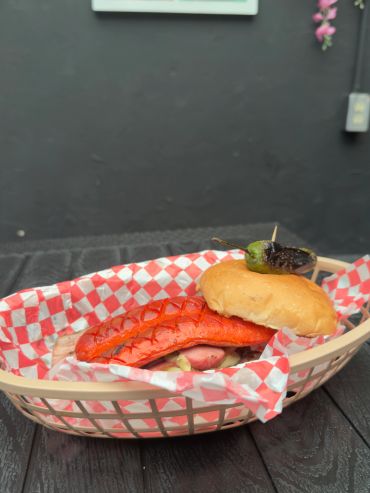 Grilled sausage sandwich with a charred jalapeño on top in a basket.
