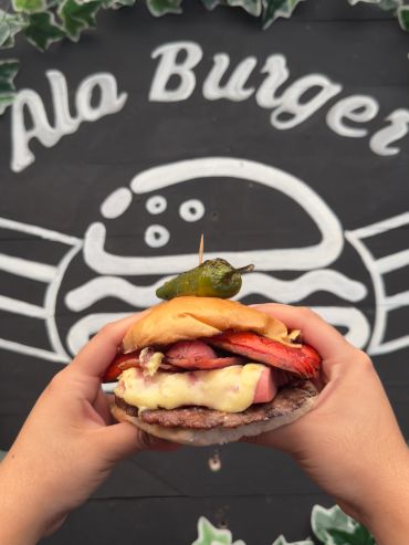 Hands holding a gourmet burger topped with a grilled pepper against a blackboard background.