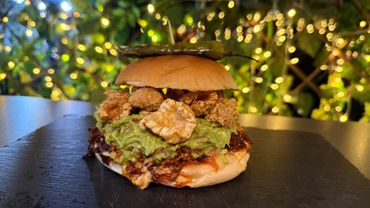 Gourmet burger with guacamole, crispy toppings, and a roasted chili on top.