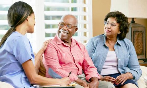 An African American female healthcare professional in blue scrubs is sitting on a couch