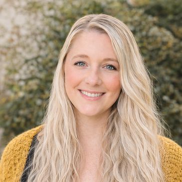 Smiling blonde woman outdoors with a yellow sweater.