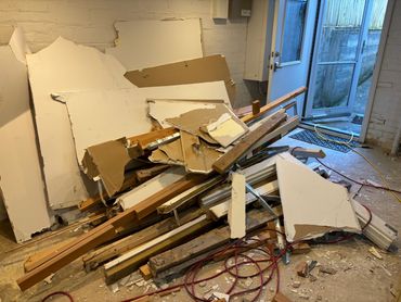 Pile of broken drywall and wood debris inside a room near an open door.