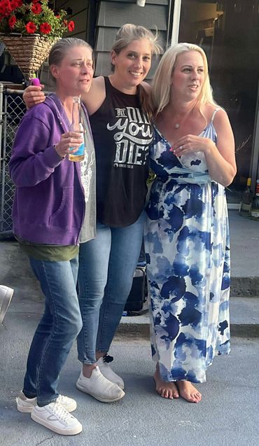 Sisters singing together outdoors, one holding a drink bottle.