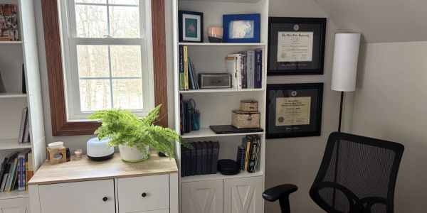 Home office with white shelves, desk, and a black chair.