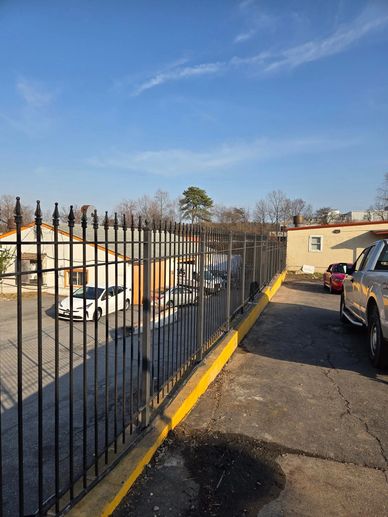 A black metal fence along a yellow curb with parked cars and buildings in the background.