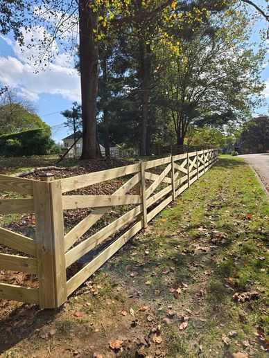 A long wooden fence runs alongside a tree-lined road on a sunny day.