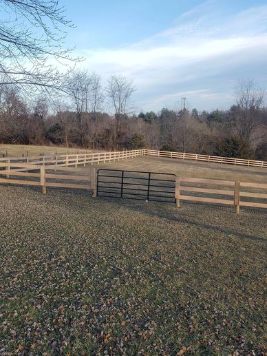 Wooden fenced pasture with a metal gate under a clear sky.
