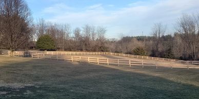 A large fenced grassy field under a blue sky with scattered clouds.