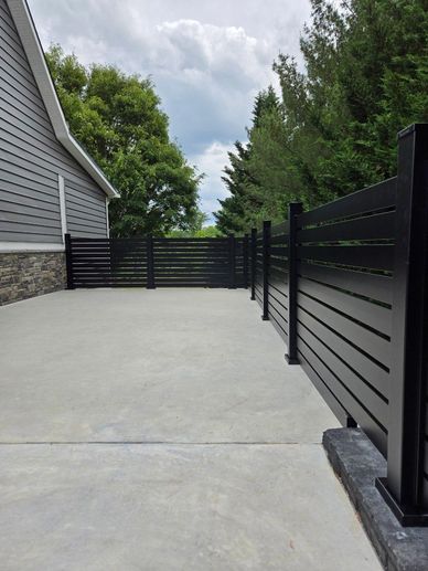 Modern black metal fence enclosing a concrete patio area beside a house.
